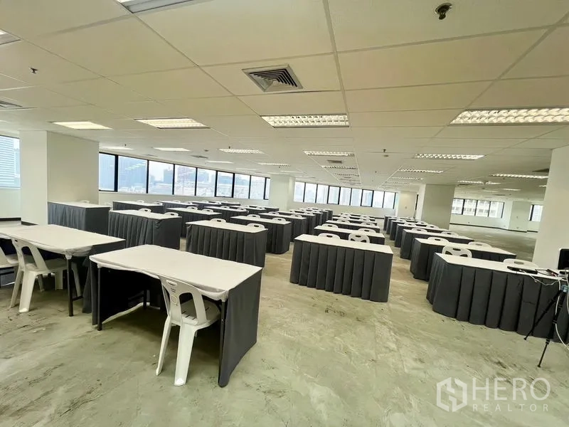 Office Space for rent - Bright office floor set up with rows of training tables and chairs beside panoramic city-view windows.