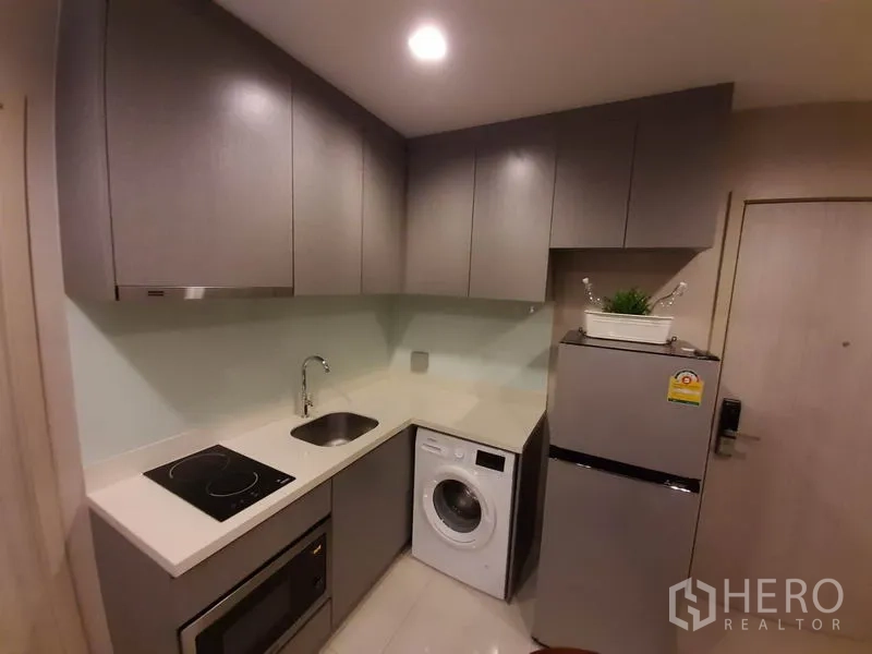 Condominium for rent or sale in Khlong Toei, Bangkok - Modern kitchen featuring induction hob, sink, washer, fridge and overhead storage.