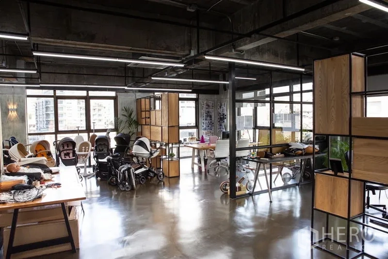 Office Space for rent in Khlong Toei, Bangkok - Open-plan industrial office with polished concrete floors, glass partitions, wood-and-metal shelving, and large windows with city views.