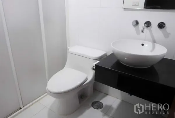 公寓 出租在Pathum Wan, Bangkok - 现代白色浴室，台上盆、壁挂龙头、坐便器与淋浴间。
