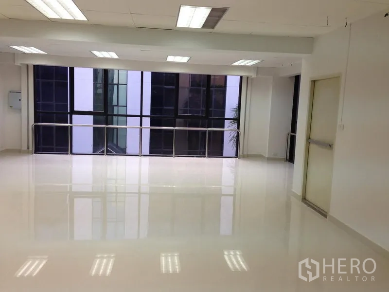 Office Space for rent in Bang Kapi, Bangkok - Clean white office floor with polished tiles, fluorescent lighting, large windows and an emergency exit door.