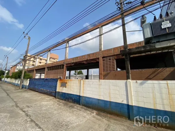 Factory for sale in Bang Phli, Samut Prakan - Roadside exterior wall and open structural frame of factory with power lines.