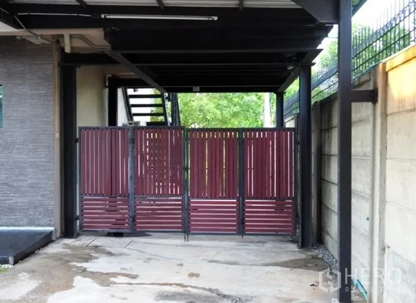 Home Office for rent in Lat Phrao, Bangkok - Side entrance with red slatted gate beneath a canopy and exterior staircase.