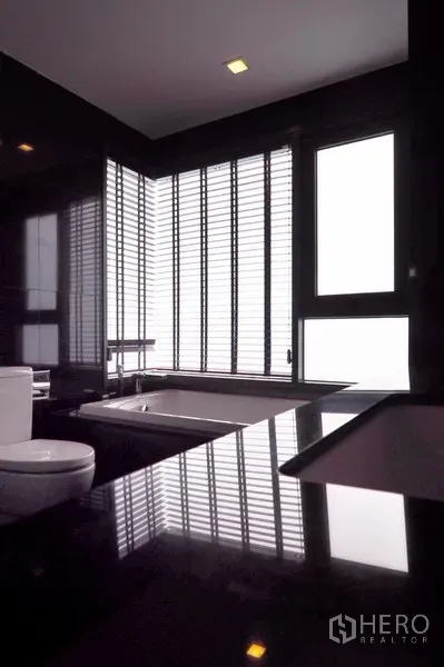 Condominium for rent in Khlong Toei, Bangkok - Modern bathroom with black stone vanity, bathtub and louvered windows.