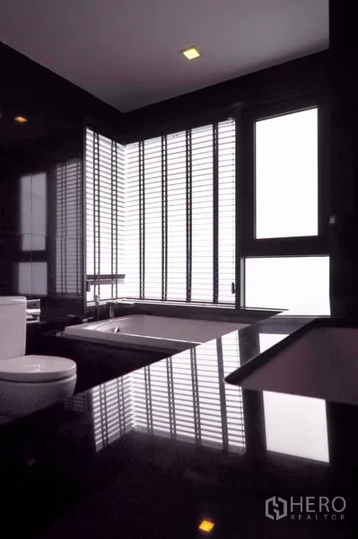 Condominium for rent in Khlong Toei, Bangkok - Modern bathroom with black stone vanity, bathtub and louvered windows.