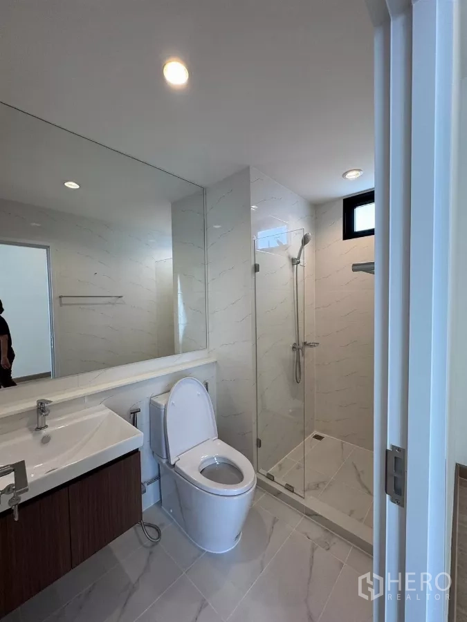 Detached House for rent in Samut Prakan - Bright bathroom with glass shower enclosure, large mirror and vanity.