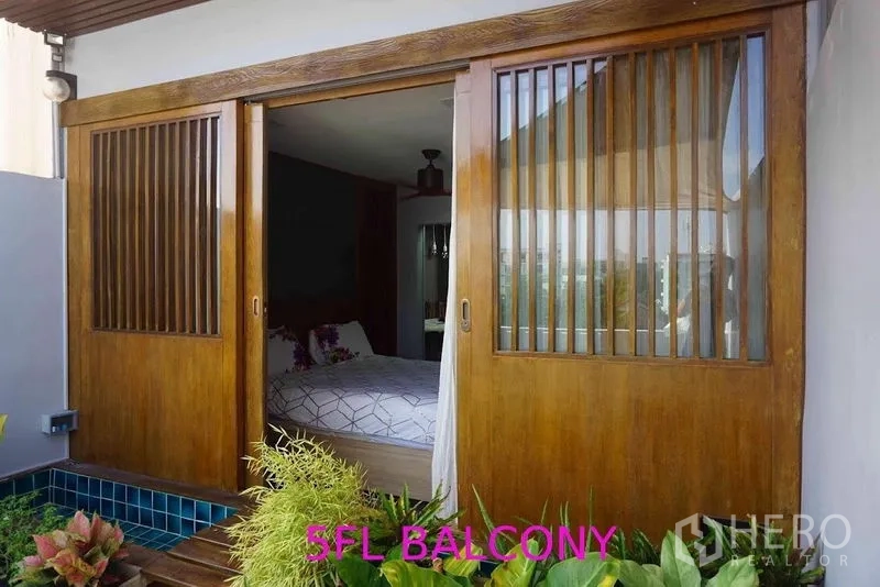 Shophouse for sale in Phra Khanong, Bangkok - Balcony garden with planters beside wooden sliding doors leading into a bedroom.