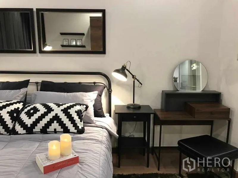 公寓 出租或出售在Ratchathewi, Bangkok - 卧室铺设柔软床品，黑白抱枕，床头灯、墙面镜与梳妆书桌。