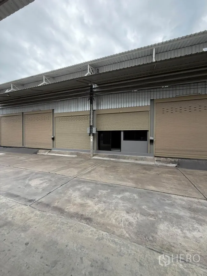 Warehouse for rent in Phra Pradaeng, Samut Prakan - Exterior frontage of the warehouse with covered loading area and several roller shutter doors.