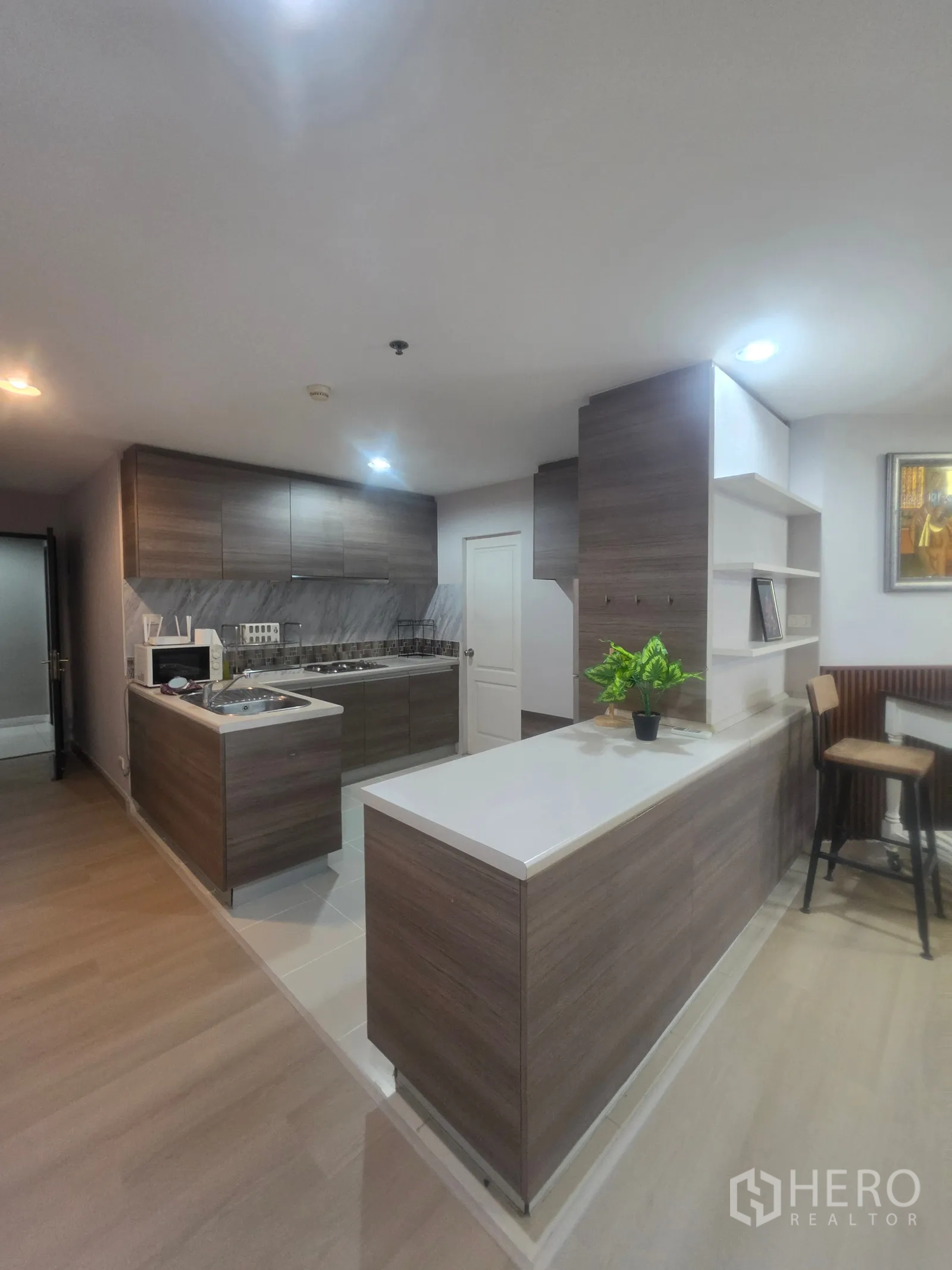 Condominium for rent in Huai Khwang, Bangkok - Modern kitchen with long counters, open shelving, and wood cabinetry.