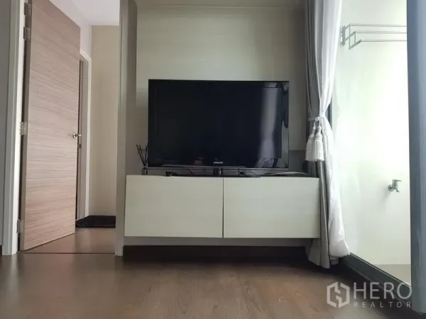 Condominium for rent in Ratchathewi, Bangkok - Flat-screen TV on a floating media console next to a floor-to-ceiling window with curtains.