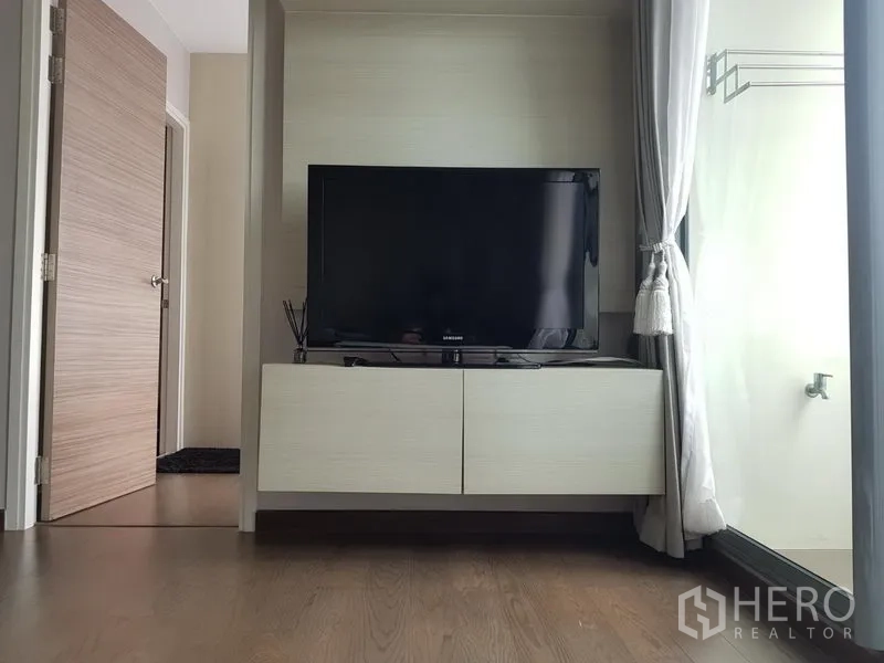 Condominium for rent in Ratchathewi, Bangkok - Flat-screen TV on a floating media console next to a floor-to-ceiling window with curtains.