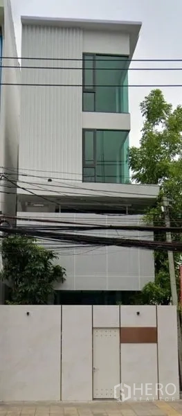 带办公室的家 出租在Suan Luang, Bangkok - 四层现代住办合一外立面，大片绿色玻璃窗与白色围墙。