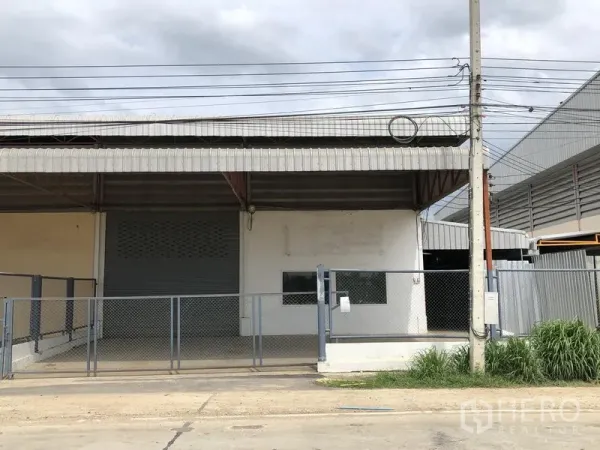 Factory for rent in Lat Lum Kaeo, Pathum Thani - Factory exterior with covered loading bay, roller shutter door and chain-link gate.