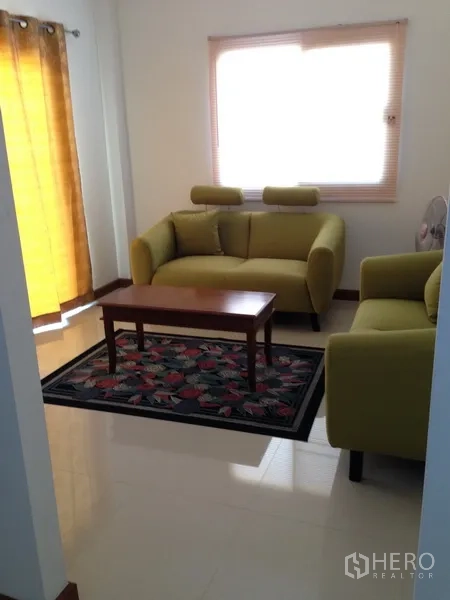 Detached House for sale in Phra Khanong, Bangkok - Bright living area with two green sofas, a coffee table and light-filtering curtains.
