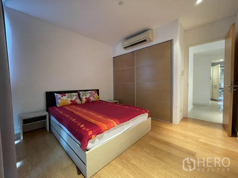 Condominium for rent or sale in Watthana, Bangkok - Second bedroom with double bed, sliding wardrobe, air conditioning, and wood floors.