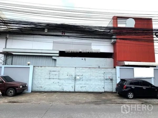 Warehouse for rent in Suan Luang, Bangkok - Street-front warehouse exterior in Suan Luang, Bangkok with high boundary wall, wide metal gate and overhead utility lines.