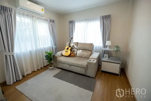 Detached House for rent or sale in Bang Phli, Samut Prakan - Bright sitting room with reclining sofa, guitars, sheer curtains and wood flooring.