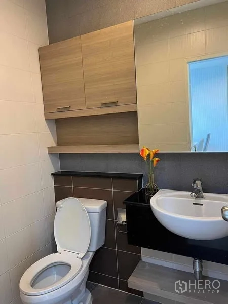 Townhouse for rent in Phra Khanong, Bangkok - Modern compact bathroom with wall cabinet, large mirror, wall-mounted basin and toilet.