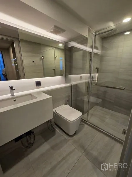 Condominium for rent - Modern bathroom with glass-enclosed shower, large mirror, and wall-hung toilet.