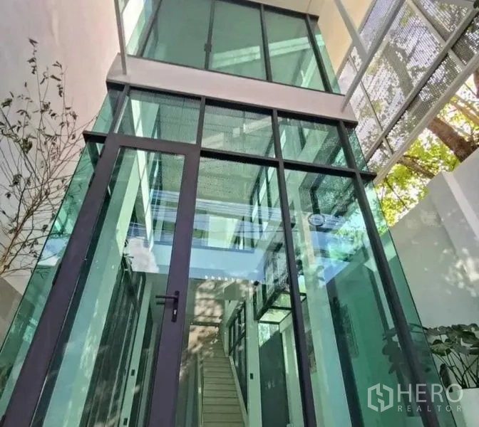 带办公室的家 出租在Suan Luang, Bangkok - 挑高玻璃中庭入口，黑色金属框架与楼梯景观。