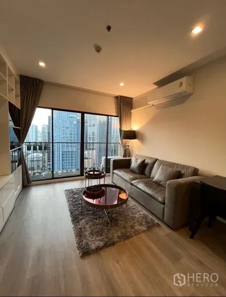 Condominium for rent in Bangkok - Cozy living room with grey sofa, floor-to-ceiling windows and city-view balcony in Khlong Toei.