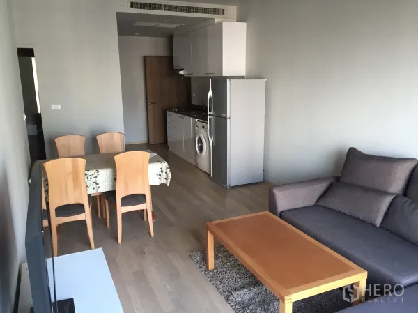 公寓 出租在Bangkok - 开放式客餐厅，配沙发、木茶几与带冰箱和洗衣机的小厨房。