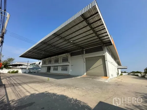Factory for rent in Samut Prakan - Large factory exterior in Bang Bo with wide steel canopy, roller shutter door, and spacious paved yard for truck loading.
