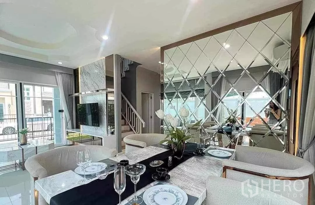 Detached House for rent in Bang Khen, Bangkok - Open‑plan living and dining area with marble TV wall, large windows and mirrored feature.