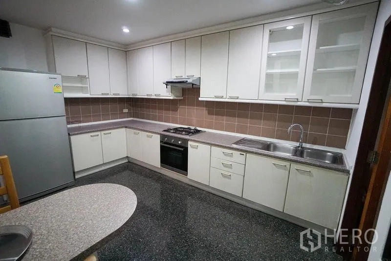 Apartment for rent in Watthana, Bangkok - Separate L-shaped kitchen with white cabinetry, gas hob and full-size fridge.