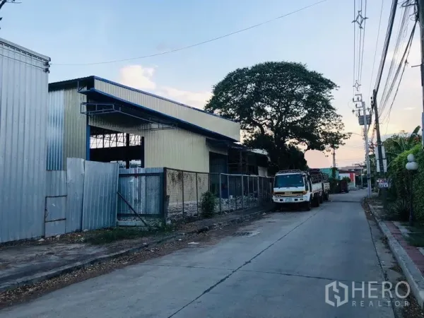 Warehouse for rent in Wang Thonglang, Bangkok - Corner angle of a metal-clad warehouse on a small industrial lane with power lines and curbside parking.