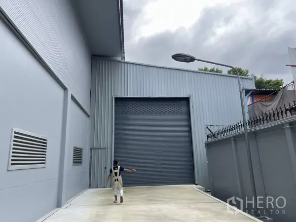 Warehouse for rent in Yan Nawa, Bangkok - Warehouse loading court with an extra‑tall roller shutter beside a secure boundary wall.