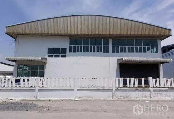 คลังสินค้า ขายในMueang Samut Prakan, Samut Prakan - ด้านหน้าโกดังสีขาวติดถนน มีรั้วเตี้ยและหน้าต่างยาวด้านบน