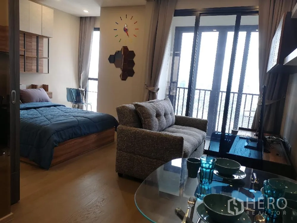 คอนโด for rent in Watthana, Bangkok - พื้นที่นั่งเล่นและนอนโปร่งสว่าง ด้วยหน้าต่างสูงจรดเพดาน เปิดออกสู่ระเบียงวิวเมือง พร้อมโซฟาและชั้นวางทีวี