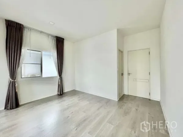 Detached House for rent in Prawet, Bangkok - Empty room with window, brown curtains, white door and wood laminate flooring.