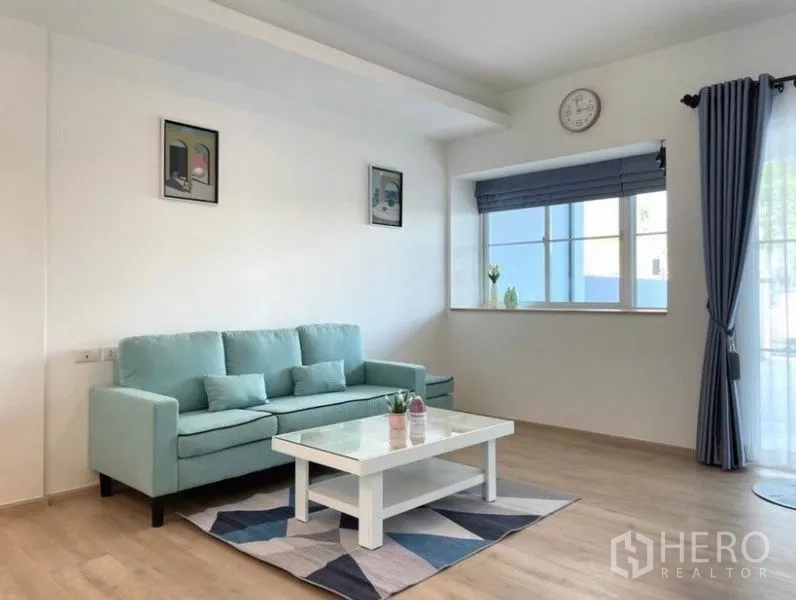联排别墅 for rent in Prawet, Bangkok - 明亮客厅配薄荷色沙发、茶几、窗户与窗帘，木地板。