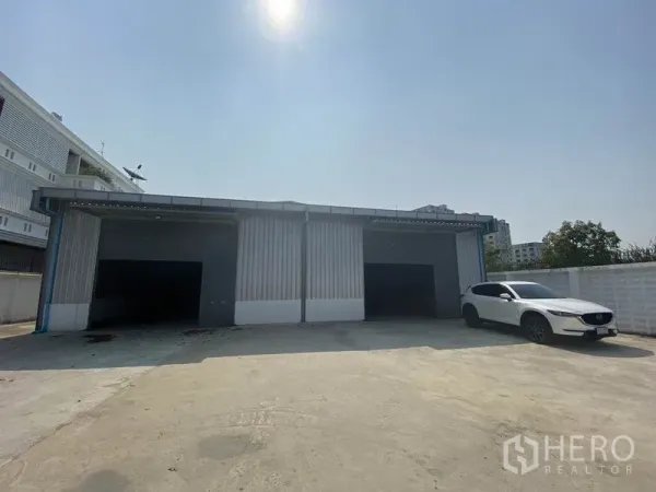 คลังสินค้า ให้เช่าในPrawet, Bangkok - ด้านหน้าโกดังผนังเมทัลชีท ประตูม้วน 3 ช่อง พร้อมลานคอนกรีตกว้าง มีรถเอสยูวีสีขาวจอด