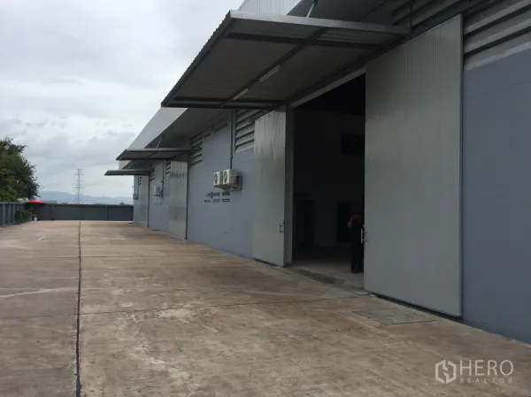 โรงงาน ให้เช่าในSi Racha, Chon Buri - ลานโหลดสินค้าด้านนอก ประตูบานสไลด์โลหะ กันสาด และทางวิ่งคอนกรีตกว้าง