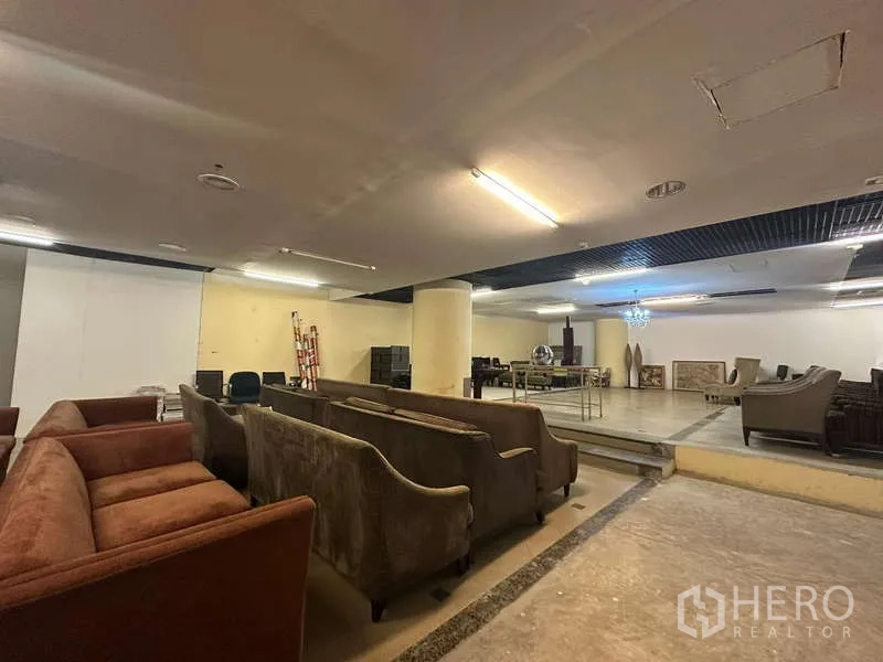 Retail Space for rent - Open-plan retail showroom with sofas, raised platform, columns and ceiling lights.
