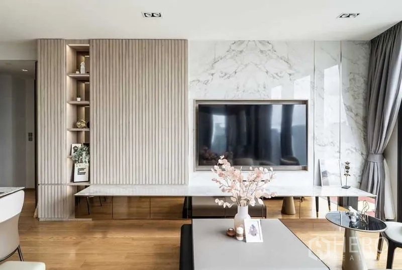 Condominium for rent in Khlong Toei, Bangkok - Contemporary TV wall with built-in shelving, marble panels, and coffee table in the living space.