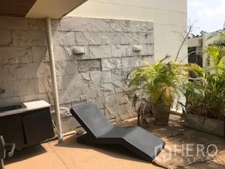 Townhouse for rent or sale in Yan Nawa, Bangkok - Private roof patio with stone-clad wall, sun lounger and greenery.
