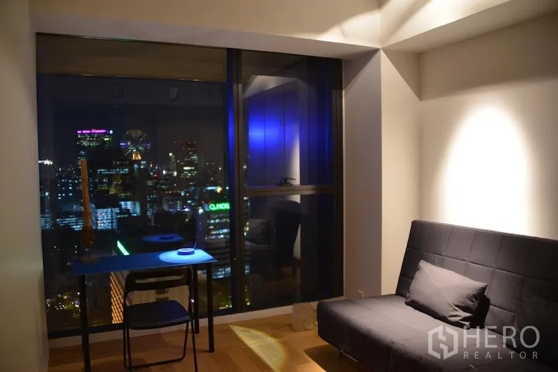 Condominium for rent or sale in Sathon, Bangkok - Multi‑purpose room with sofa bed and desk facing the nighttime skyline through a large window.