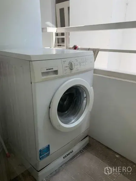 Condominium for rent in Khlong Toei, Bangkok - Front‑loading washing machine on a covered utility balcony with railing.