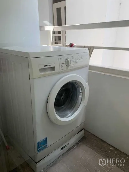 Condominium for rent in Khlong Toei, Bangkok - Front‑loading washing machine on a covered utility balcony with railing.