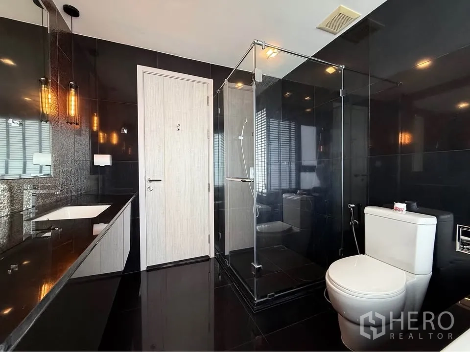 公寓 for rent in Khlong Toei, Bangkok - 时尚深色瓷砖浴室，带玻璃淋浴、马桶与长台面洗手台。