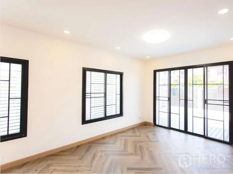 Detached House for sale in Wang Thonglang, Bangkok - Bright living area with large sliding glass doors, black-framed windows and herringbone flooring.