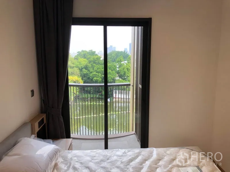 Condominium for rent in Watthana, Bangkok - Second bedroom with single bed and sliding door to small balcony overlooking canal and greenery.