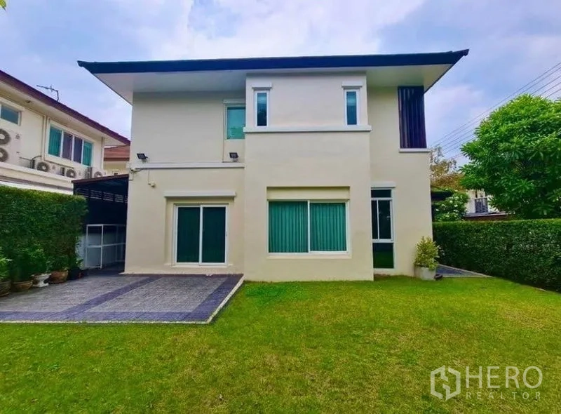 Detached House for rent or sale in Lat Krabang, Bangkok - Rear view of modern two-storey house with large windows, driveway and lawn.