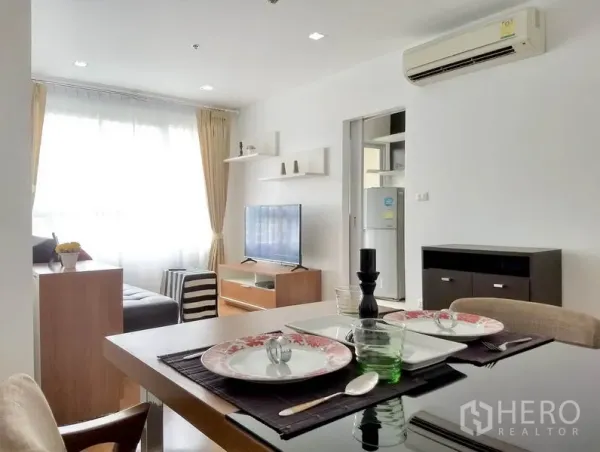 Condominium for rent or sale in Khlong Toei, Bangkok - Open-plan dining and lounge with set table, floating shelves, flat-screen TV and air conditioner.
