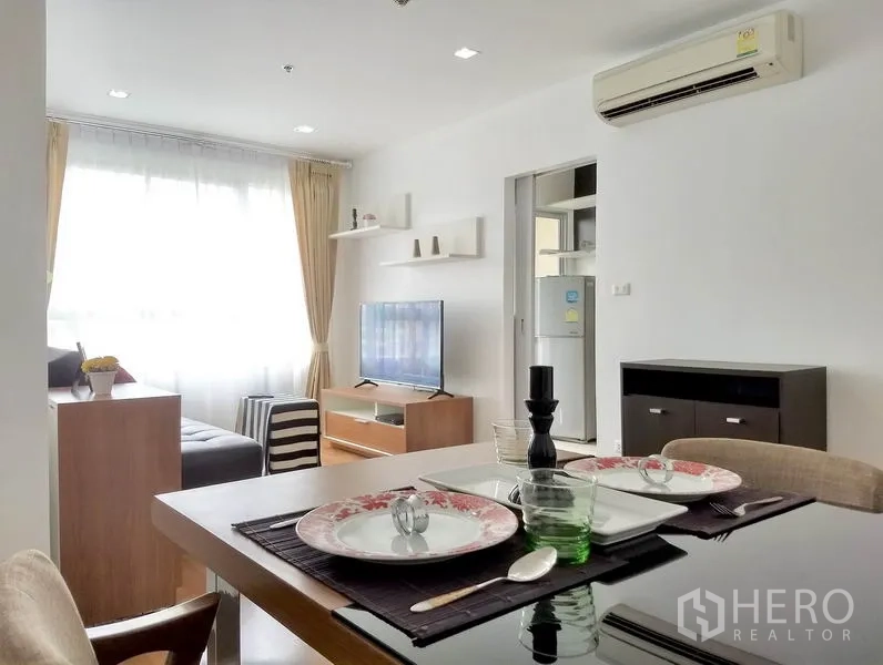 Condominium for rent or sale in Khlong Toei, Bangkok - Open-plan dining and lounge with set table, floating shelves, flat-screen TV and air conditioner.